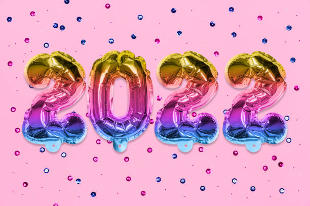 istock Rainbow foil balloon number, digit 2022 on a pink background with colored sequins. New Year's card. 1351482051
