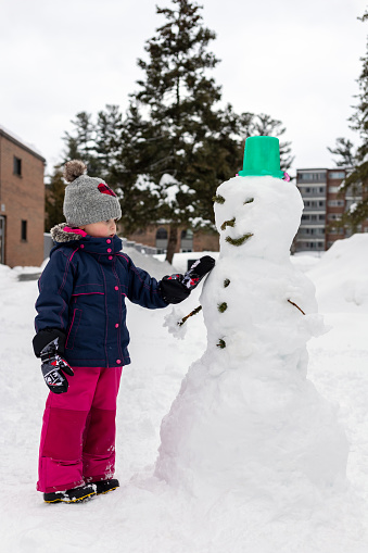 Small child making snowman, playing outdoors with snow on snowy cold winter day. Girl wearing snowsuit, having fun.