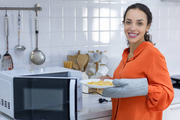 woman cooking in microwave in kitchen stock photo