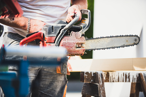 Man sawing a wooden beam with a chain saw, close up