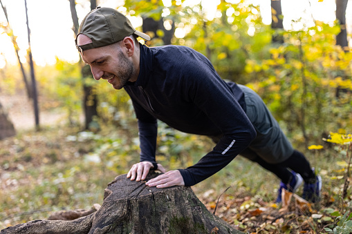 A young man doing tight push-ups in nature with the help of a stump