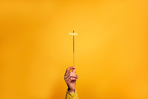 Female hand holding a sparkler light on a yellow background - Christmas, new year, birthday and celebration concept
