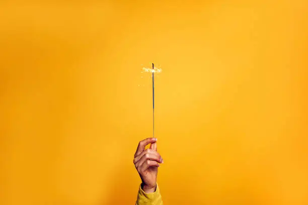 Photo of Female hand holding a sparkler light on a yellow background - Christmas, new year, birthday and celebration concept