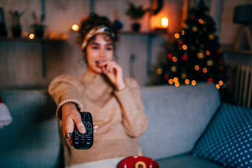Young woman watching a movie in the living room at night during cozy Christmas holidays