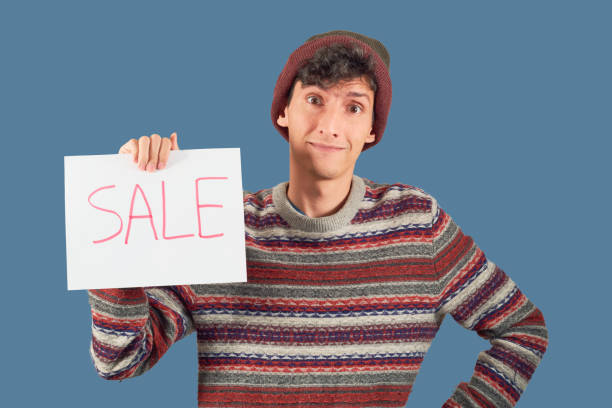 Young man in sweater shows winter sales in isolation on flat background with copy space.