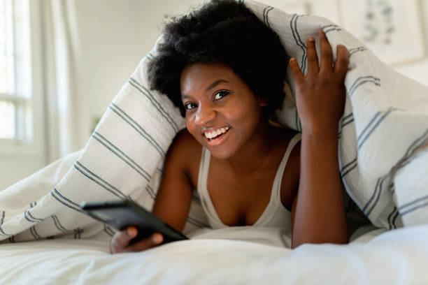 istock Young African Woman Lying On Bed Using Mobile Phone 1351490105