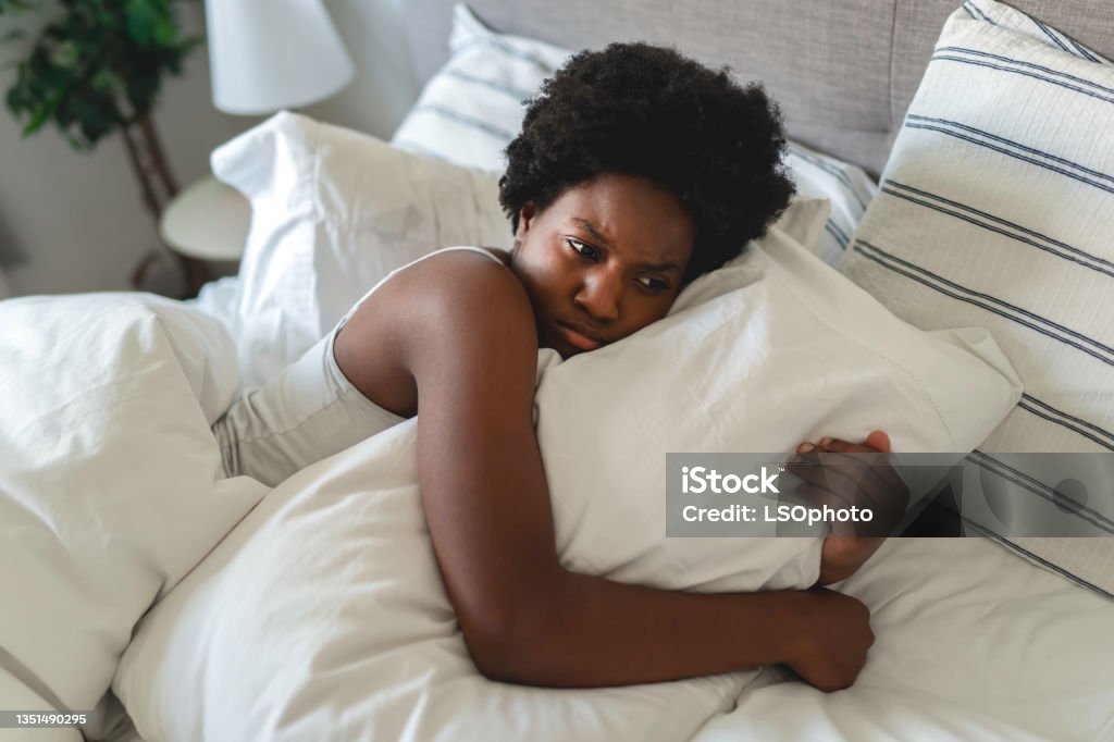 beautiful young African woman in tank top lying in bed look sad with his pillow A beautiful young African woman in tank top lying in bed look sad with his pillow Women Stock Photo