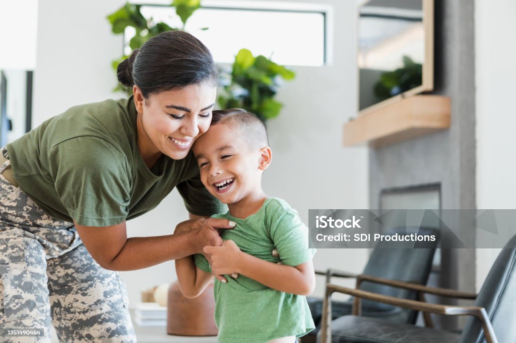 Solder embraces young son A cheerful female soldier smiles as she embraces her little boy while relaxing at home. Veteran Stock Photo