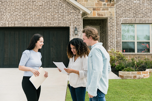 The cheerful mid adult female real estate agent gives the mid adult couple a paper listing the of features of the house for sale.