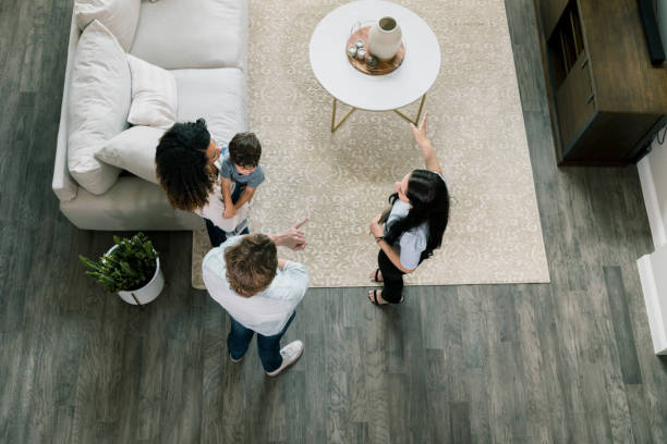 High angle view real estate agent showing house to family A high angle view as a female real estate agent shows the living room of the model home to the young family of three. estate agent stock pictures, royalty-free photos & images