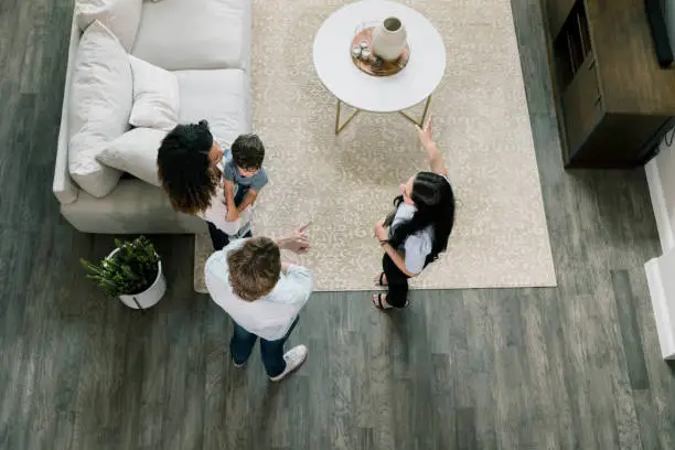 A high angle view as a female real estate agent shows the living room of the model home to the young family of three.