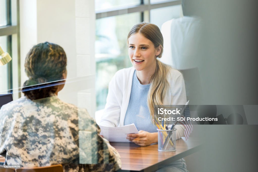 Excited young woman meets with female army recruiter While at a military recruitment office, an excited young woman talks with a military officer. Officer - Military Rank Stock Photo