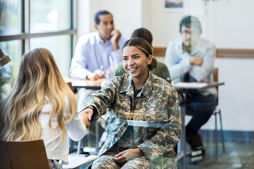 A young female soldier greets a female military counselor with a handshake. The soldier is seeking counseling in a military counseling center.