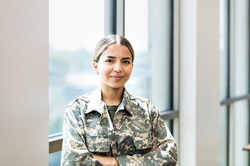 A confident female soldier stands with her arms crossed while working in a recruitment office.