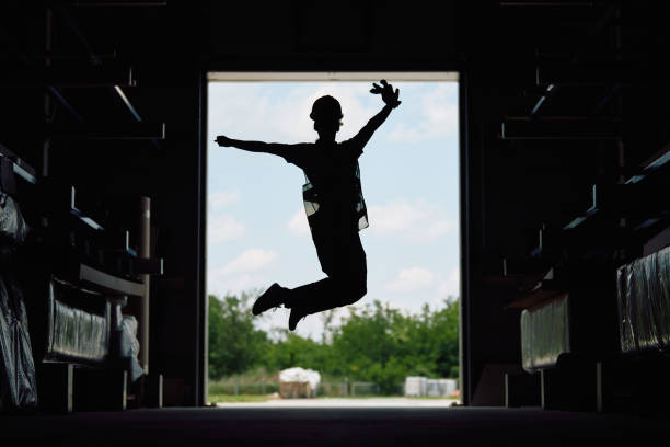 Silhouette of female worker having fun and jumping with arms outstretched in a warehouse.