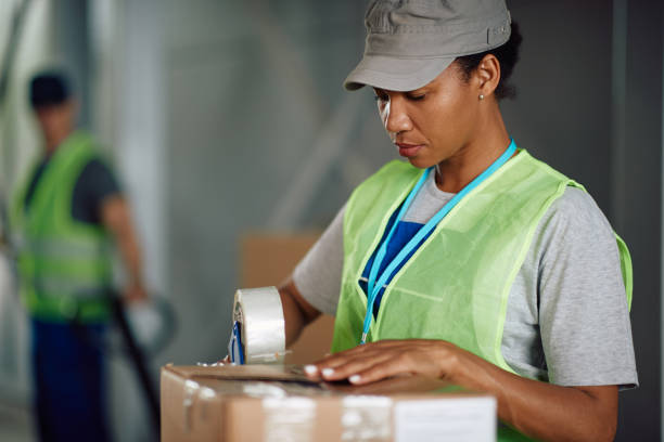 istock Black female worker taping carboard boxes while working in a warehouse. 1351492582