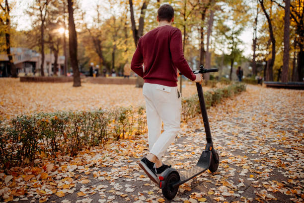 Man pushes a scooter through a park covered with leaves