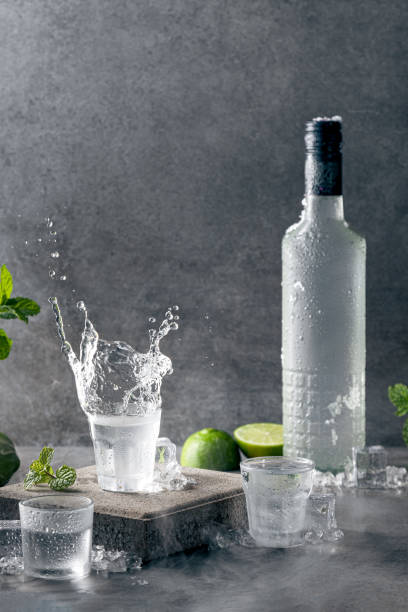 bottiglia di vodka con splash shot glass su sfondo cemento con copyspace.. formato verticale. - martini brand vermouth foto e immagini stock