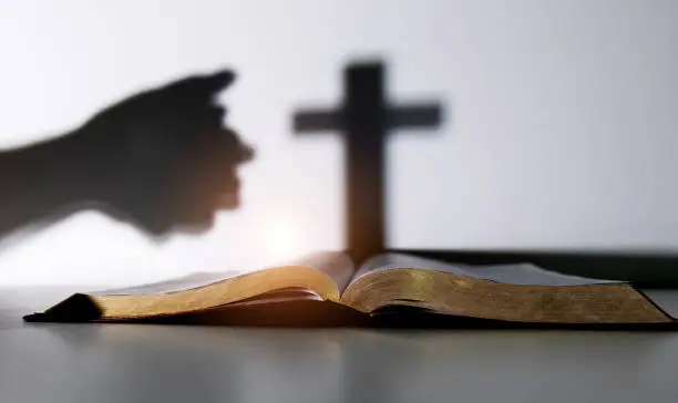 Silhouette of human hand praying with a cross.