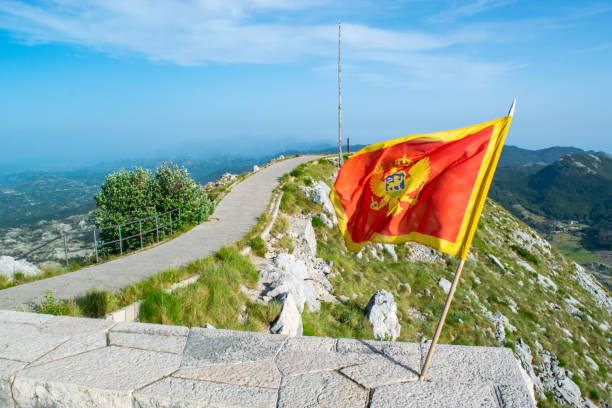 wehende flagge von montenegro vor dem hintergrund der berge, in der nähe des njegos-mausoleums im nationalpark lovcen. montenegro. sommerblaue montanlandschaft. - lovcen stock-fotos und bilder
