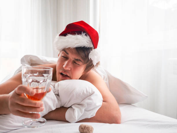 Man in Santa hat is trying to freshen the nip after alco party. He is suffering of headache after New Year or Christmas celebration. Heavy morning. Alcohol withdrawal. Worst hangover. stock photo