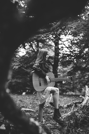 Portrait of a beautiful little girl playing a Spanish guitar in the forest. Monochrome version.