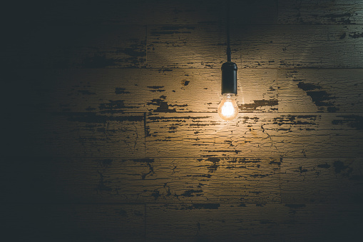 Vintage light bulb hanging against weathered wooden wall in the darkness