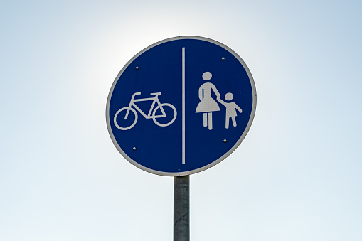A shared path traffic sign in front of the clear blue sky. A round blue metal plate in Germany. This symbol shows that cyclists and pedestrians share a footpath and should be careful.