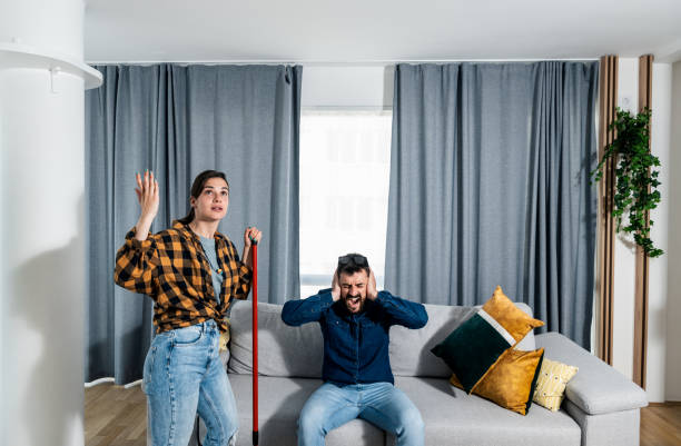 Young couple stares at the ceiling and yells because a neighbor upstairs is having a party with loud music or renovating an apartment and workers are drilling with heavy tools. Noise pollution concept una pareja joven mira al techo y grita porque un vecino de arriba está teniendo una fiesta con música a todo volumen o renovando un apartamento y los trabajadores están perforando con herramientas pesadas. concepto de contaminación acústica