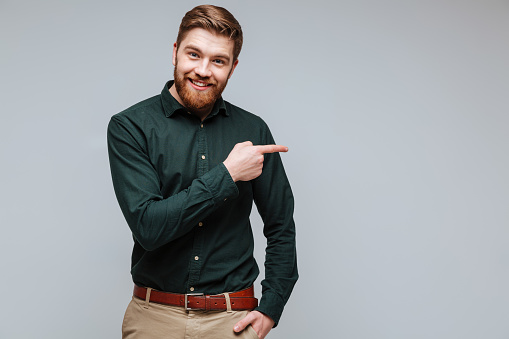 Smiling Bearded man in green shirt and with arm in pocket pointing away