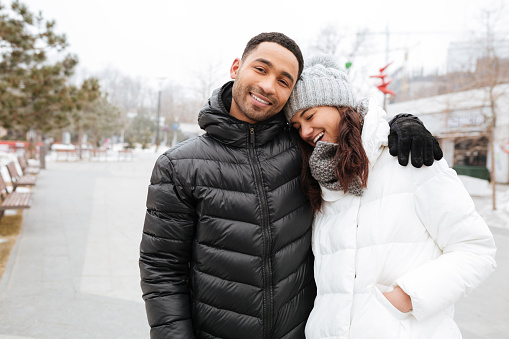 Happy multiethnic young couple hugging and laughing in winter park