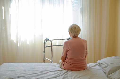 Elderly woman in nursing home room holding walking frame with wrinkled hand. Senior lady grabbing metal walker's handles. Interior background, copy space, close up.