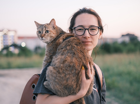 Young woman walking with cute ginger cat in the city park on summer evening.