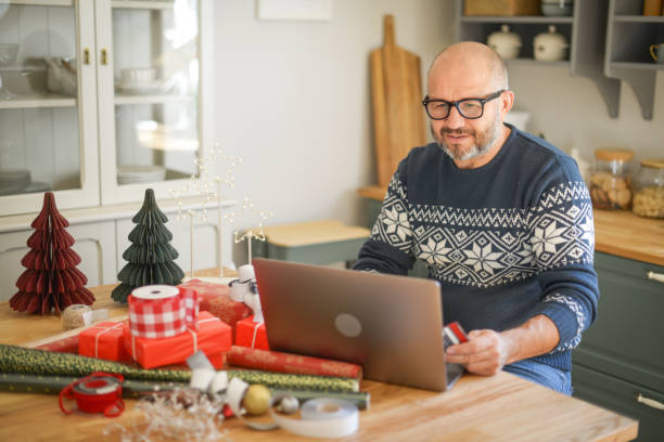 reifer erwachsener mann im weihnachtlichen zuhause (online-shopping) - holiday shopping fotos stock-fotos und bilder