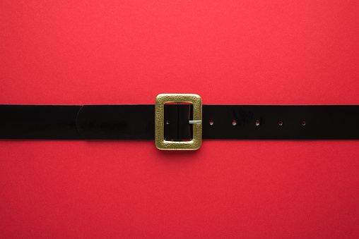 Creative Christmas composition. Overhead flat lay view photo of Santa Claus black belt with golden buckle on bright color red backdrop