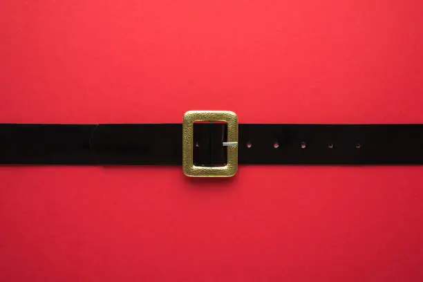 Creative Christmas composition. Overhead flat lay view photo of Santa Claus black belt with golden buckle on bright color red backdrop
