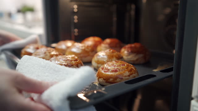 Woman taking out freshly baked buns from the oven in a modern kitchen.