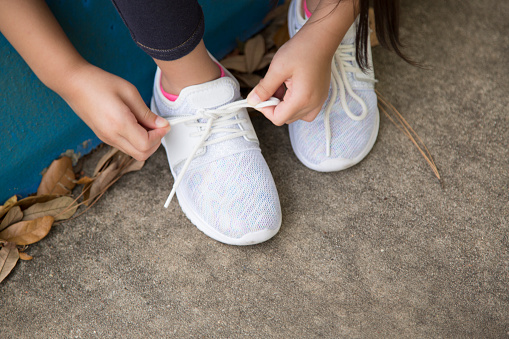 Various ages of children gather in front of school.   Tying her shoes.