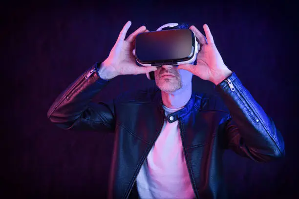 Smiling man dressed casual watching content in virtual reality glasses with dark isolated background