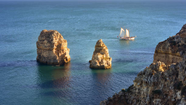 istock Sail boat sailing past rocky coast 1351554091