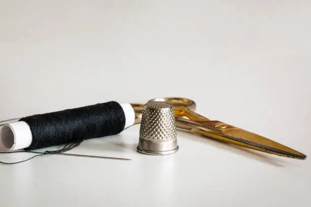 Thimble, needle, black thread and a pair of scissors. Basic sewing tool.
