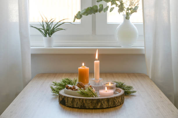 Advent and Christmas decoration, four different lit candles on a rustic wooden tray with fir branches and cookies on a table at the window, copy space stock photo
