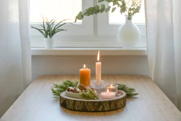 Advent and Christmas decoration, four different lit candles on a rustic wooden tray with fir branches and cookies on a table at the window, copy space, selected focus, narrow depth of field