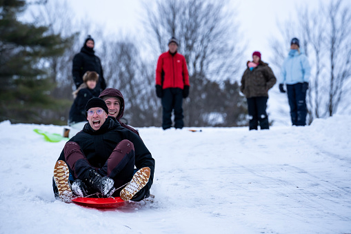 A young gay couple tobogganing with their family during winter in Quebec.