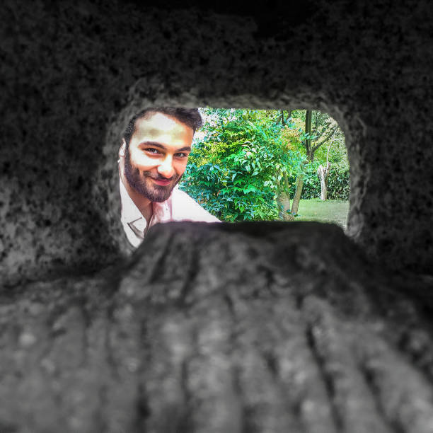 a young man looking at camera in front of some trees in a green area and frame showing a rocky place