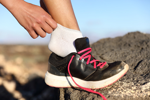 Runner putting on fitness shoes and running shoes adjusting socks closeup outdoors on mountain background. Female athlete getting ready for marathon race preparing her feet on trail run.