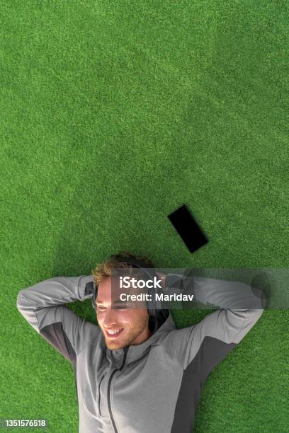 Listening To Music For Relaxation Happy Man Lying Down On Grass Enjoying Podcast On Mobile Phone With Wireless Headphones Summer Lifestyle Stock Photo - Download Image Now