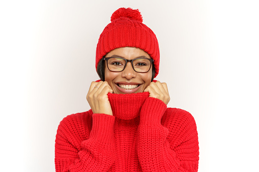 Funny woman wearing warm knitted hat and sweater happy smiling. Young african american woman dressed winter in clothes and eyeglasses ready to wintertime weather, cold and frost, isolated studio shot