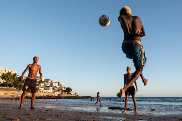 jóvenes jugando al fútbol de arena al atardecer en la playa de ondina - beach football fotografías e imágenes de stock