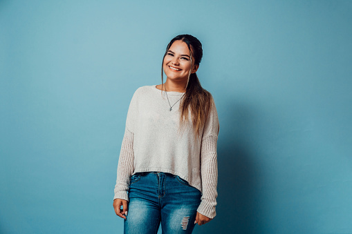 portrait of cheerful young woman latinx with casual clothes smiling looking at camera stand over blue background.